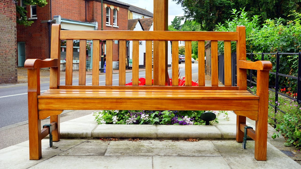 A wooden bench is placed in an urban street surrounded by vibrant flowers.