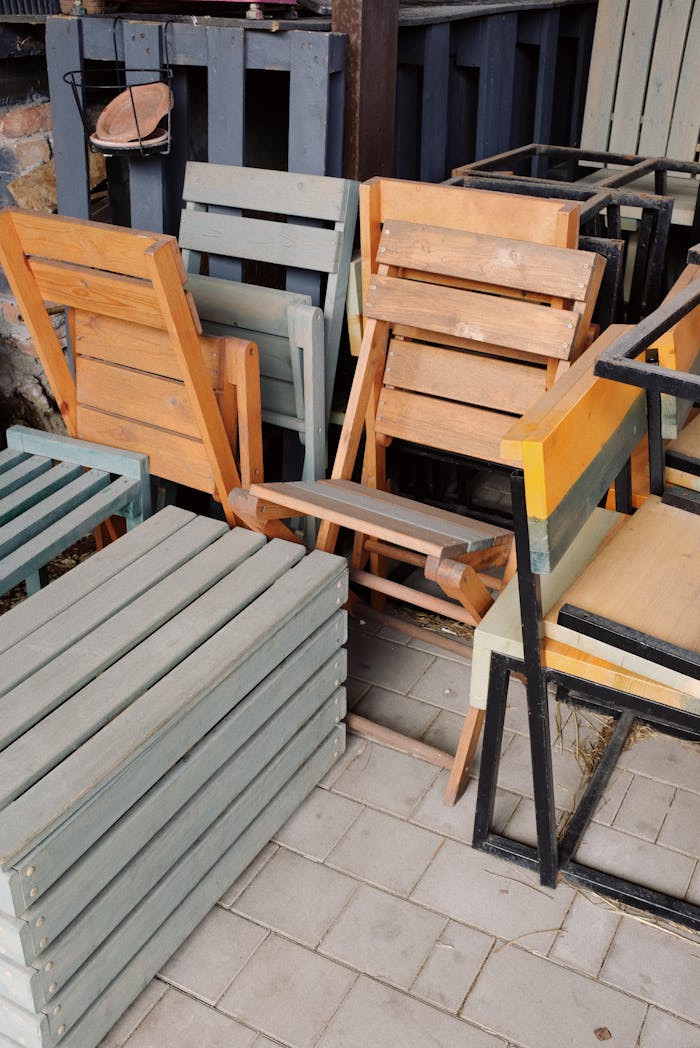 A collection of assorted wooden chairs stacked outside, showcasing various designs and colors.