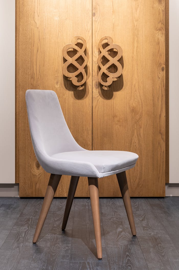 Comfortable single chair with wooden legs placed on parquet near big closet with decorative handles in modern apartment at home